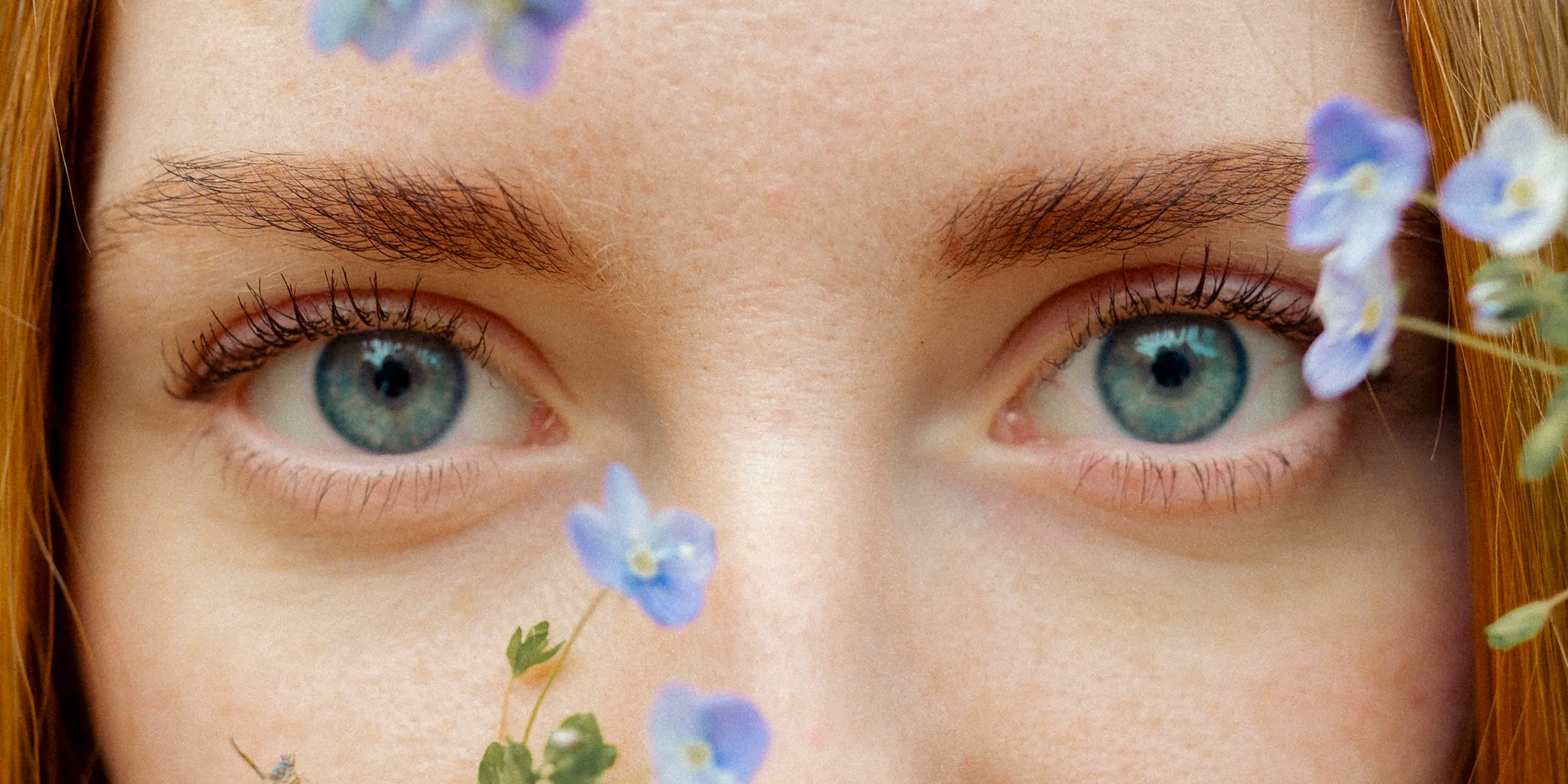Close-up of a woman's blue eyes framed by small blue flowers