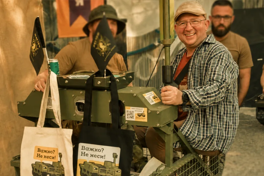 Smiling man at a charity stand with military equipment and printed tote bags