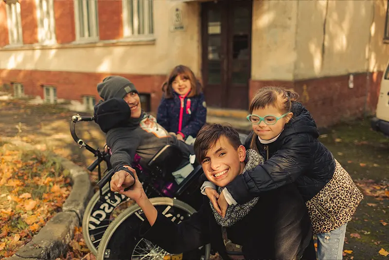 Children laughing together around a child in a wheelchair in an autumn courtyard